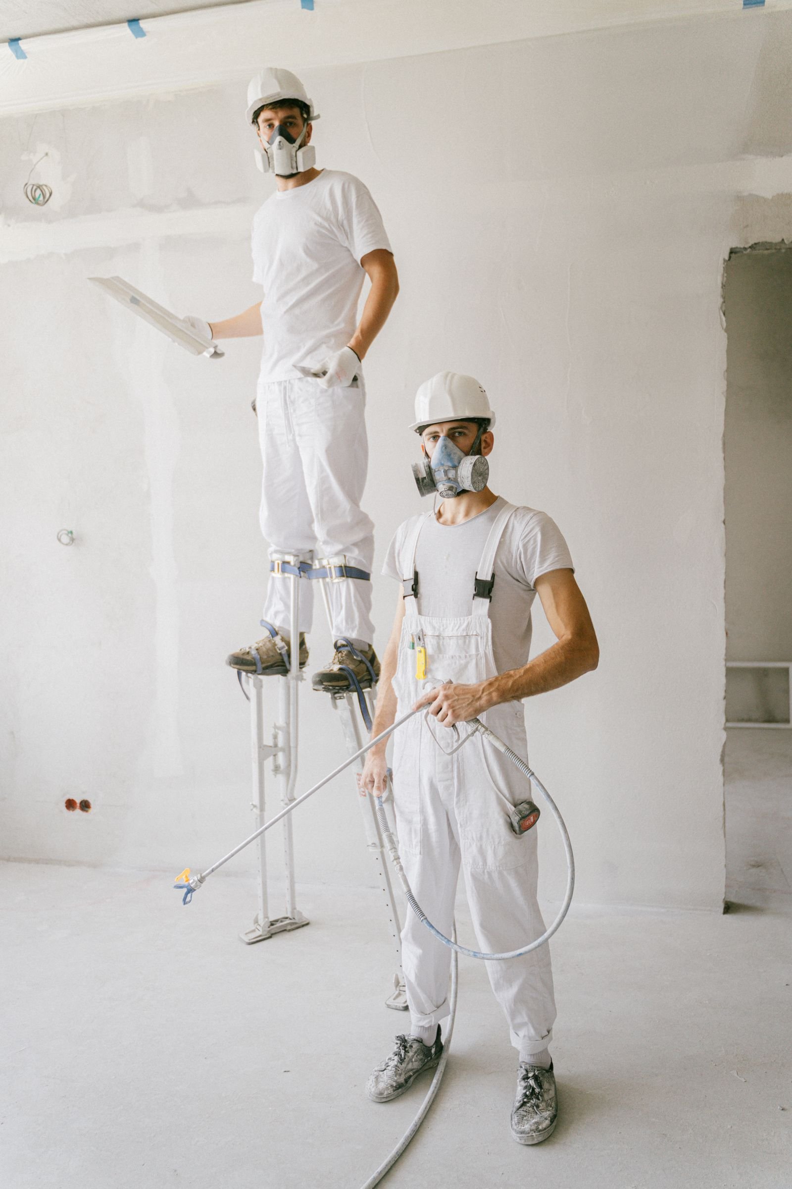 Painters in protective gear with a paint sprayer