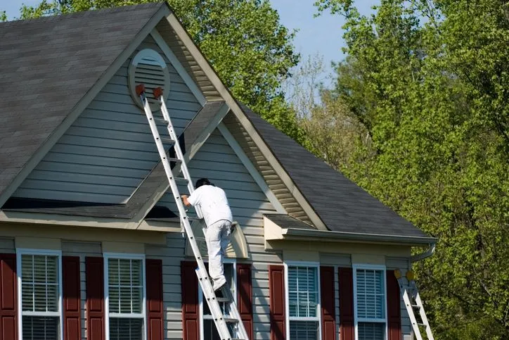 Painter on a ladder refreshing the trim of a two-story home