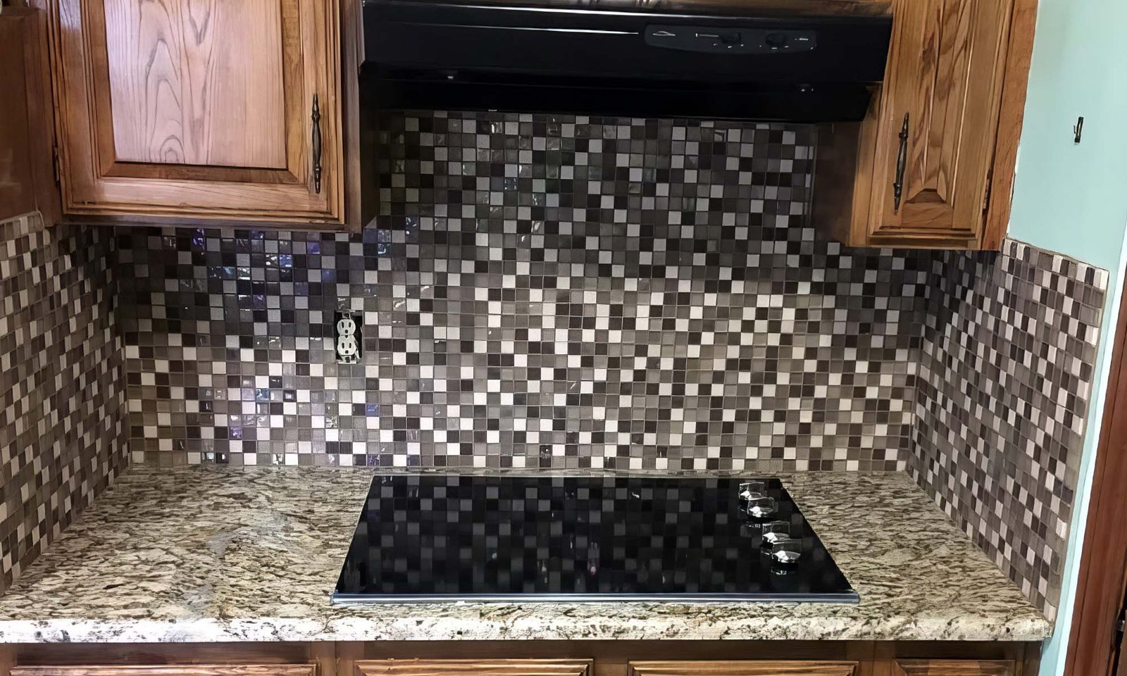 Glass mosaic kitchen backsplash over granite with cooktop